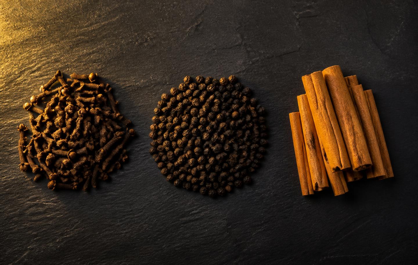 Cloves, black peppercorns and cinnamon quills arranged on dark slate